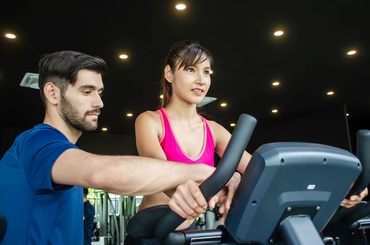 Une femme sur un vélo de sport assisté par un coach sportif